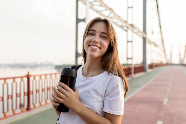 橋の上の魔法瓶を持って笑顔の旅行女性の正面図