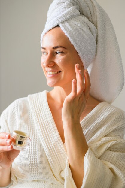 Front view of smiley woman applying cream on her face at home