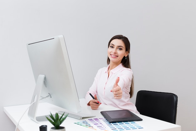 Front view of smiley woman at desk giving thumbs up