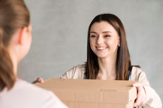 Front view of smiley woman handing cardboard box to customer