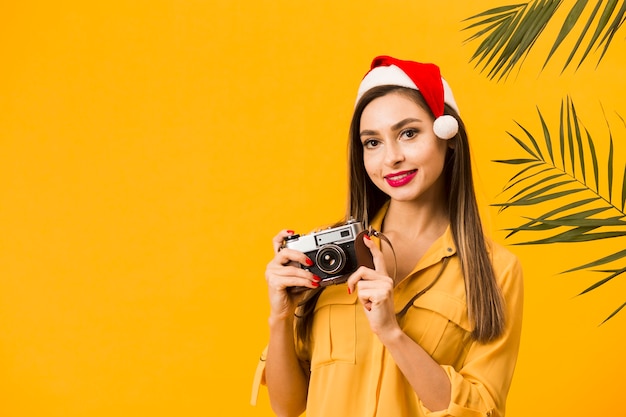 Foto gratuita vista frontale della macchina fotografica della tenuta della donna di smiley mentre porta il cappello di santa con lo spazio della copia