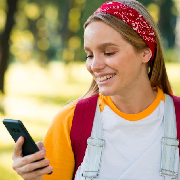 スマートフォンを屋外で見ている笑顔の女性の正面図