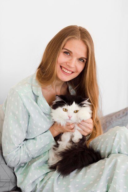 Front view of smiley woman in pajamas holding cat