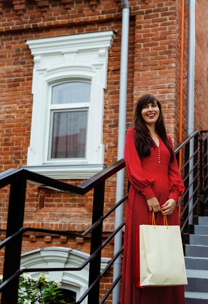 Front view of smiley woman posing outdoors with shopping bags