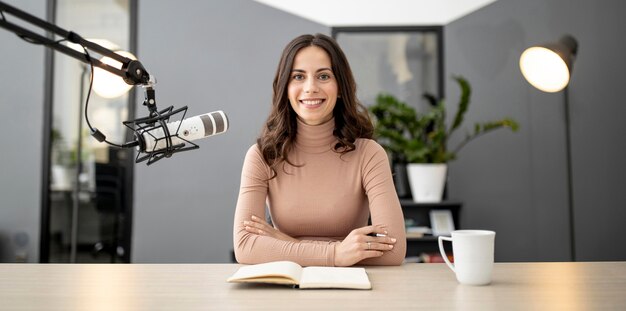 Front view of smiley woman on the radio with microphone and notebook