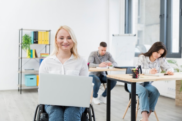 Front view of smiley woman in wheelchair posing with laptop at work