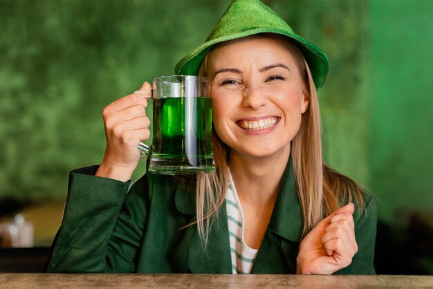 Vista frontale della donna sorridente con il cappello che celebra st. patrick's day con drink