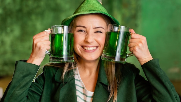 Front view of smiley woman with hat celebrating st. patrick's day with drinks