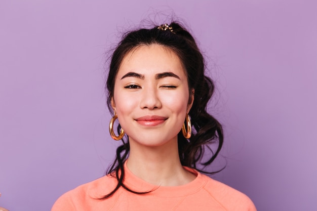 Vista frontale della donna asiatica sorridente in orecchini. studio shot di gioiosa signora cinese isolata su sfondo viola.