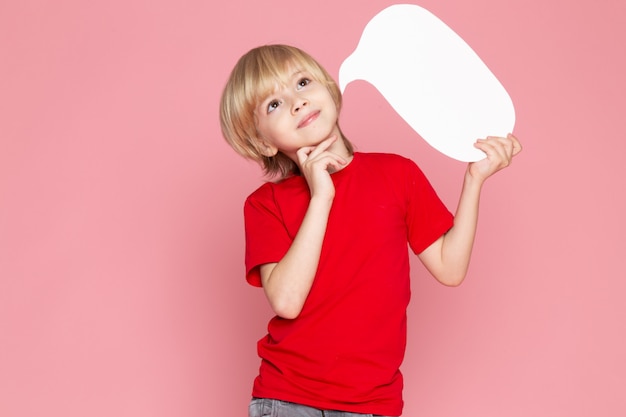 Free photo a front view smiling blonde boy holding white sign in red t-shirt on the pink space