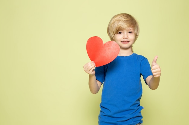 A front view smiling boy in blue t-shirt holding heart shaped figure on the stone colored space