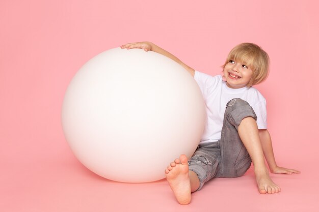분홍색 바닥에 흰색 둥근 공을 가지고 노는 흰색 티셔츠에 전면보기 웃는 소년