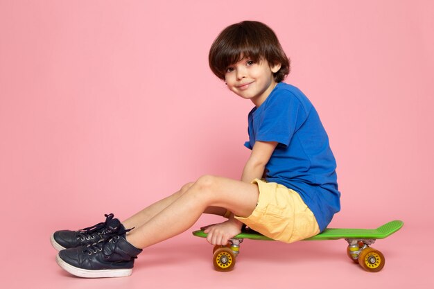 A front view smiling cute boy in blue t-shirt riding skateboard on the pink floor