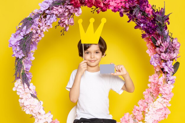 A front view smiling cute boy in white t-shirt around colorful flowers on the yellow space