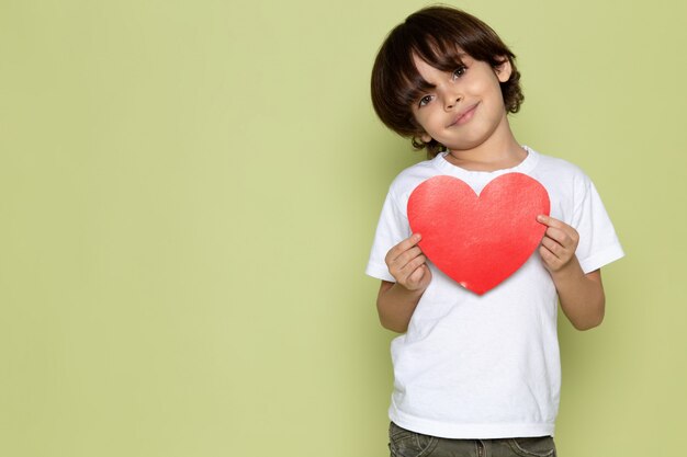 A front view smiling cute boy in white t-shirt and holding heart shape on the stone colored space