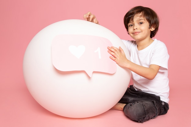 A front view smiling cute boy in white t-shirt playing with white round ball on the pink space