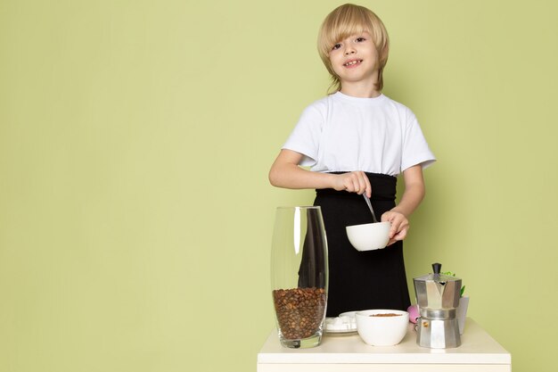 石色のスペースでコーヒーを飲む準備をして白いtシャツのかわいい男の子を笑顔の正面図