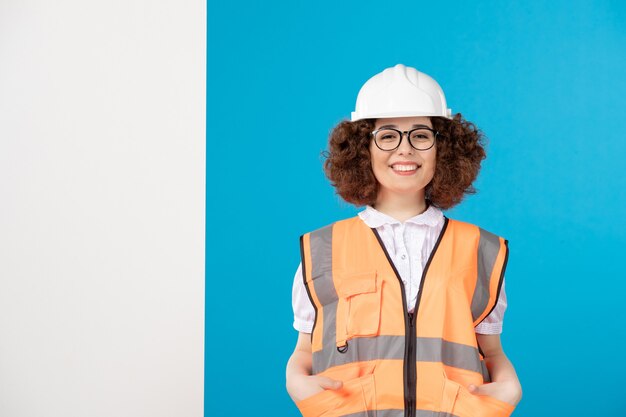 Вид спереди улыбается женщина-строитель в униформе на синем
