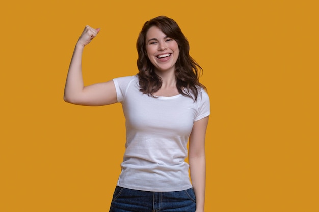 Front view of a smiling fit dark-haired girl flexing her arm muscles before the camera