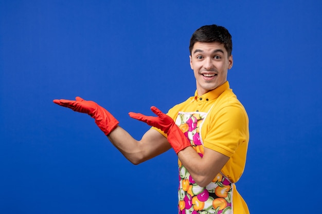 Front view of smiling housekeeper man reaching out his hands standing on blue wall