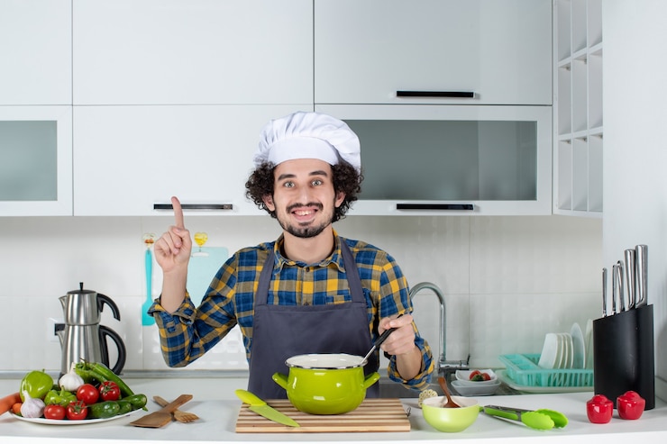 मुफ़्त फोटो front view of smiling male chef with fresh vegetables tasting ready meal and pointing up in the white kitchen