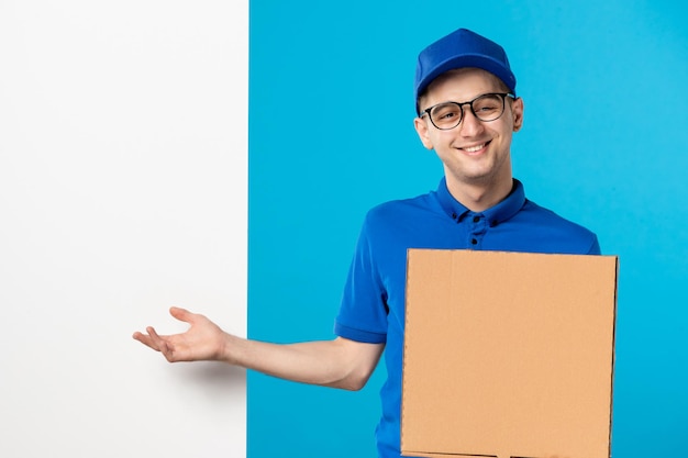 Front view of smiling male courier in blue uniform with pizza on blue 