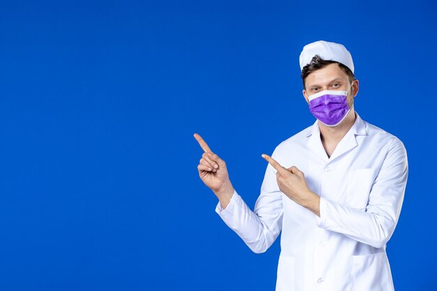Front view of smiling male doctor in medical suit and purple mask on blue 