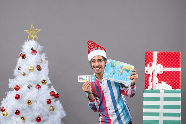 Front view smiling man with santa hat holding world map and travel ticket