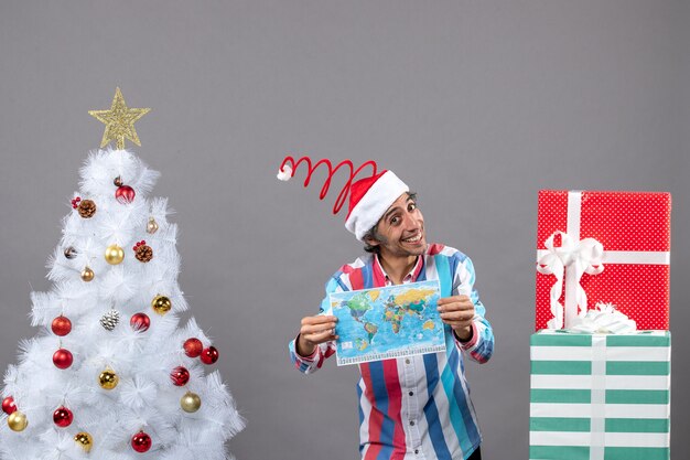 Front view smiling man with spiral spring santa hat holding world map