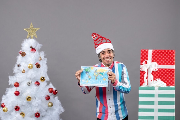 Front view smiling man with spiral spring santa hat and striped shirt holding map