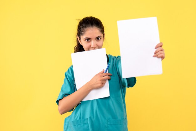 Front view smiling pretty female doctor holding papers on yellow background