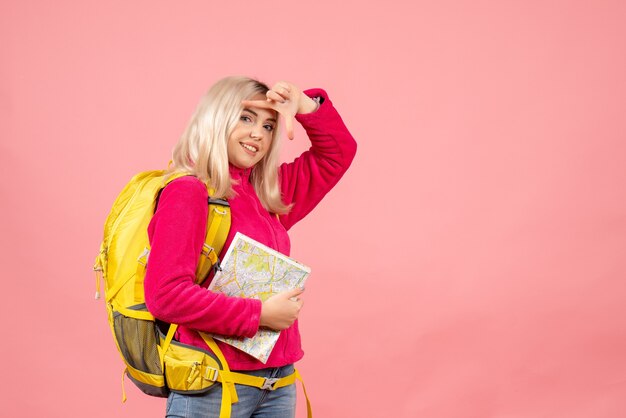 Front view smiling traveler woman with backpack holding map on pink wall