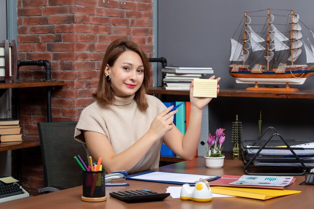 Front view of smiling woman holding note paper working in office