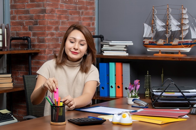 Front view smiling woman taking highlighter sitting at wall