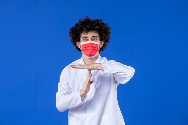 Вид спереди улыбающегося молодого врача в медицинском костюме с красной маской на синем