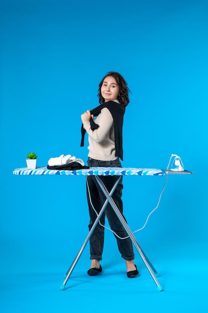 Front view of smiling young girl standing behind the iron board checking cloth on blue wave background