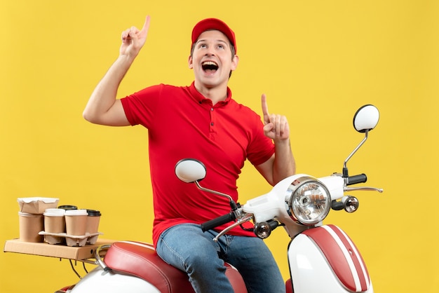 Вид спереди улыбающегося молодого парня в красной блузке и шляпе, доставляющего заказы на желтом фоне