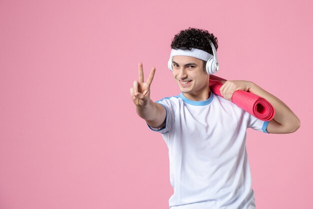 Front view smiling young male in sport clothes with yoga mat