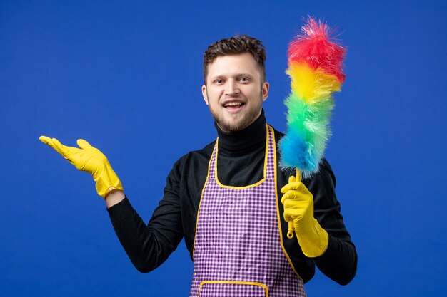 Front view of smiling young man holding dust brush on blue wall