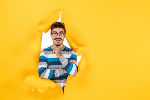 Вид спереди улыбающегося молодого человека, смотрящего через разорванную бумажную желтую стену