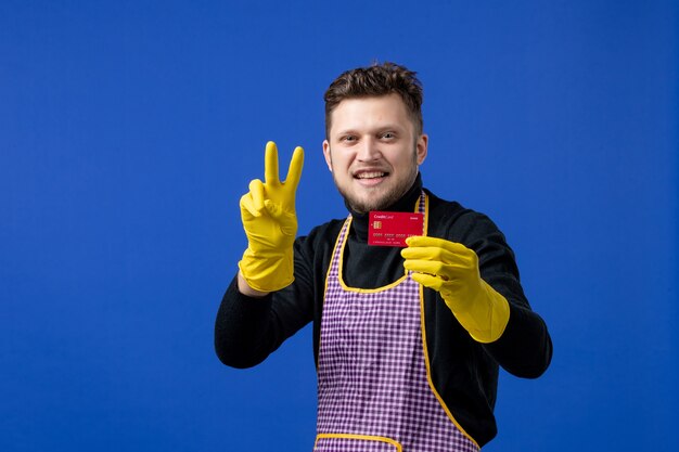 Front view of smiling young man making victory sign on blue wall