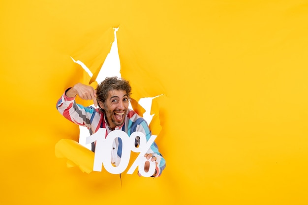 Free photo front view of smiling young man pointing ten percentage in a torn hole in yellow paper