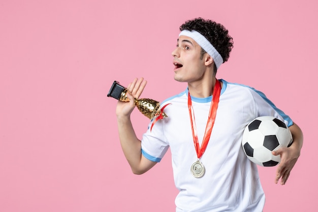 Вид спереди футболист в спортивной одежде с золотым кубком и медалью