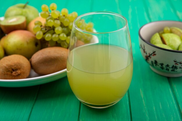 녹색 배경에 접시에 녹색 사과 키위 녹색 포도와 배와 유리에 전면보기 청량 음료