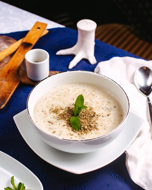 A front view soup decorated with green leaf inside white plate on the blue surface