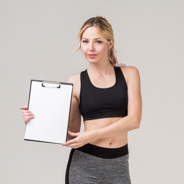 Front view of sporty woman posing while holding notepad