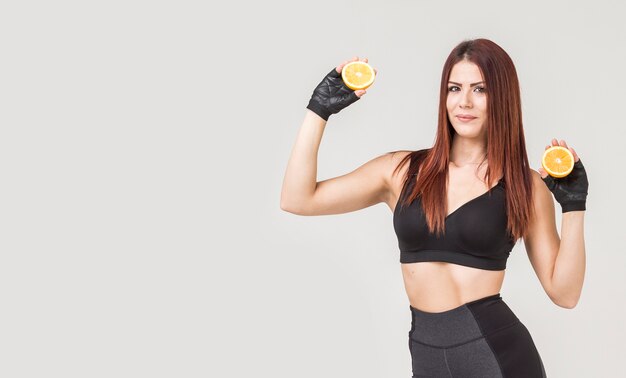 Front view of sporty woman posing with oranges