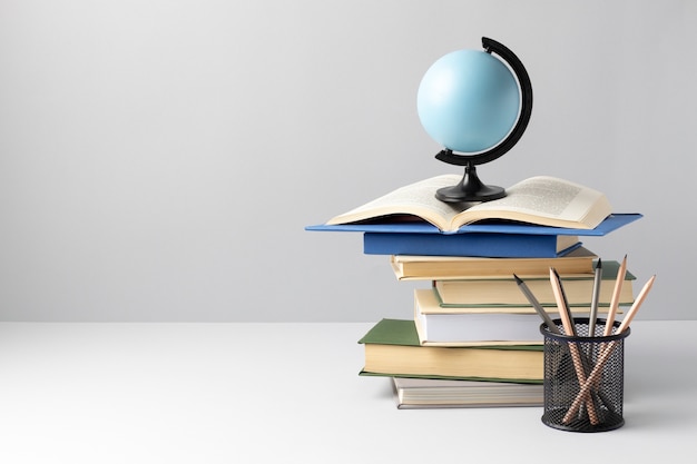 Front view of stacked books, an earth globe, an open book and pencils for education day