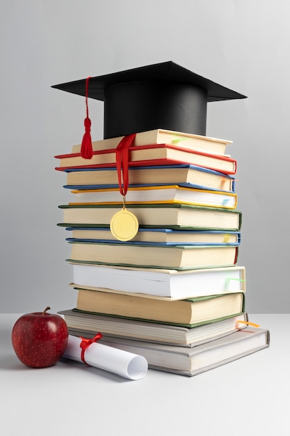 Front view of stacked books, a graduation cap and a diploma for education day