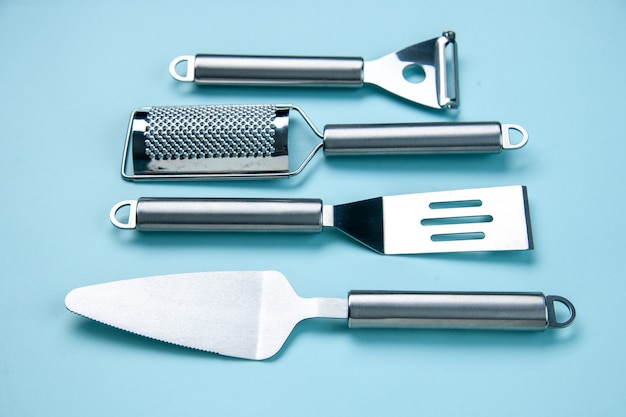 Front view of stainless kitchen tools lying side by side on soft blue wave background with free space